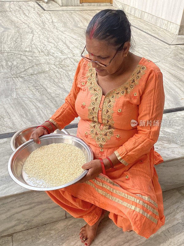 特写图像:印度妇女在不锈钢塔利(金属托盘)里洗米，用水淘白米，盘腿坐在大理石楼梯台阶上，穿着Salwar Kameez传统服装和眼镜，重点在前景